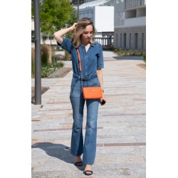 Sac Lou orange , sac pochette en cuir avec chainette porté en bandoulière croisé sur une combinaison en jean bleue